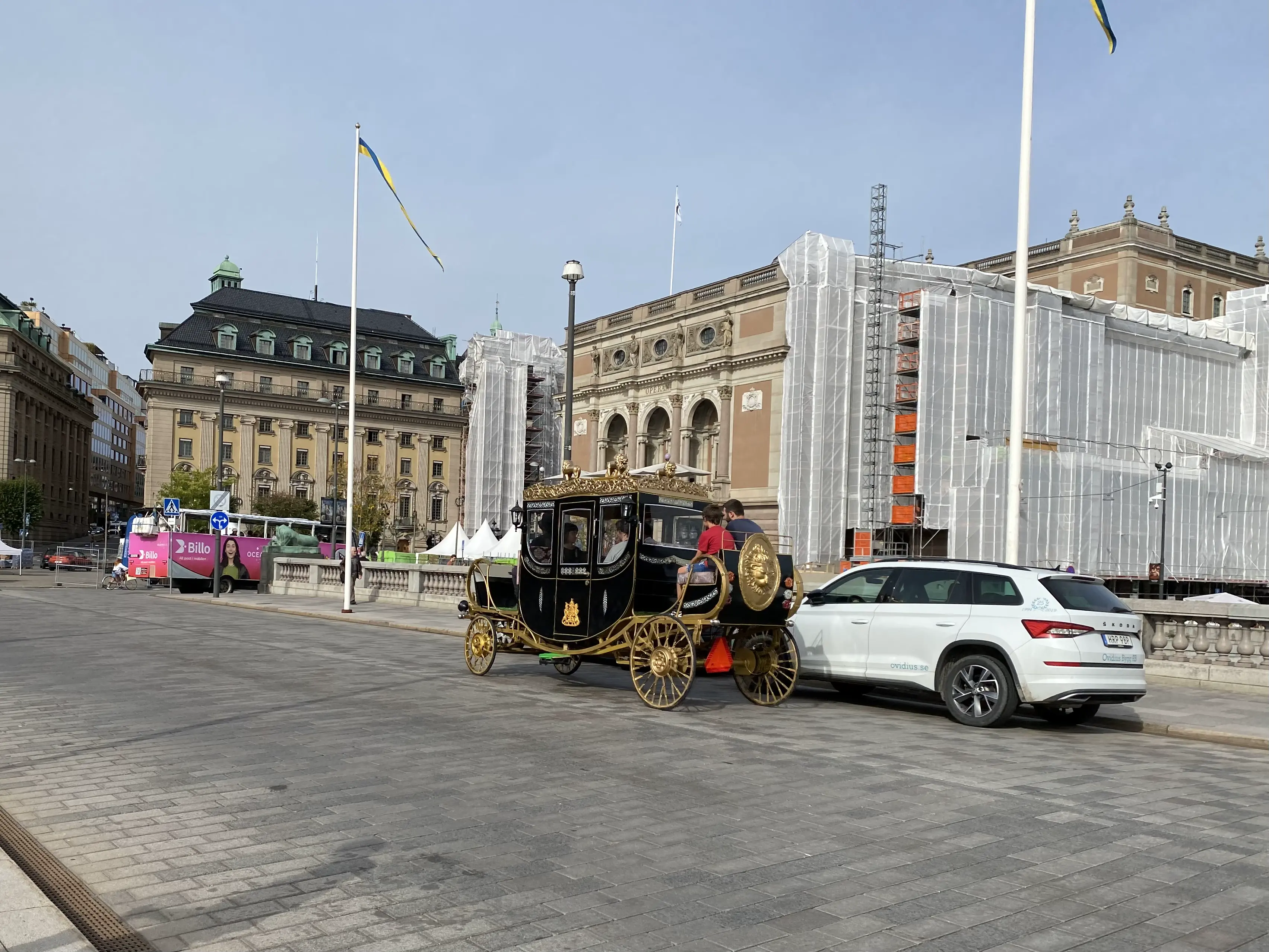 Foto einer elektrischen Kutsche auf einer breiten Strasse. Im Hintergrund sieht man Gebaeude der Stockholmer Innenstadt.